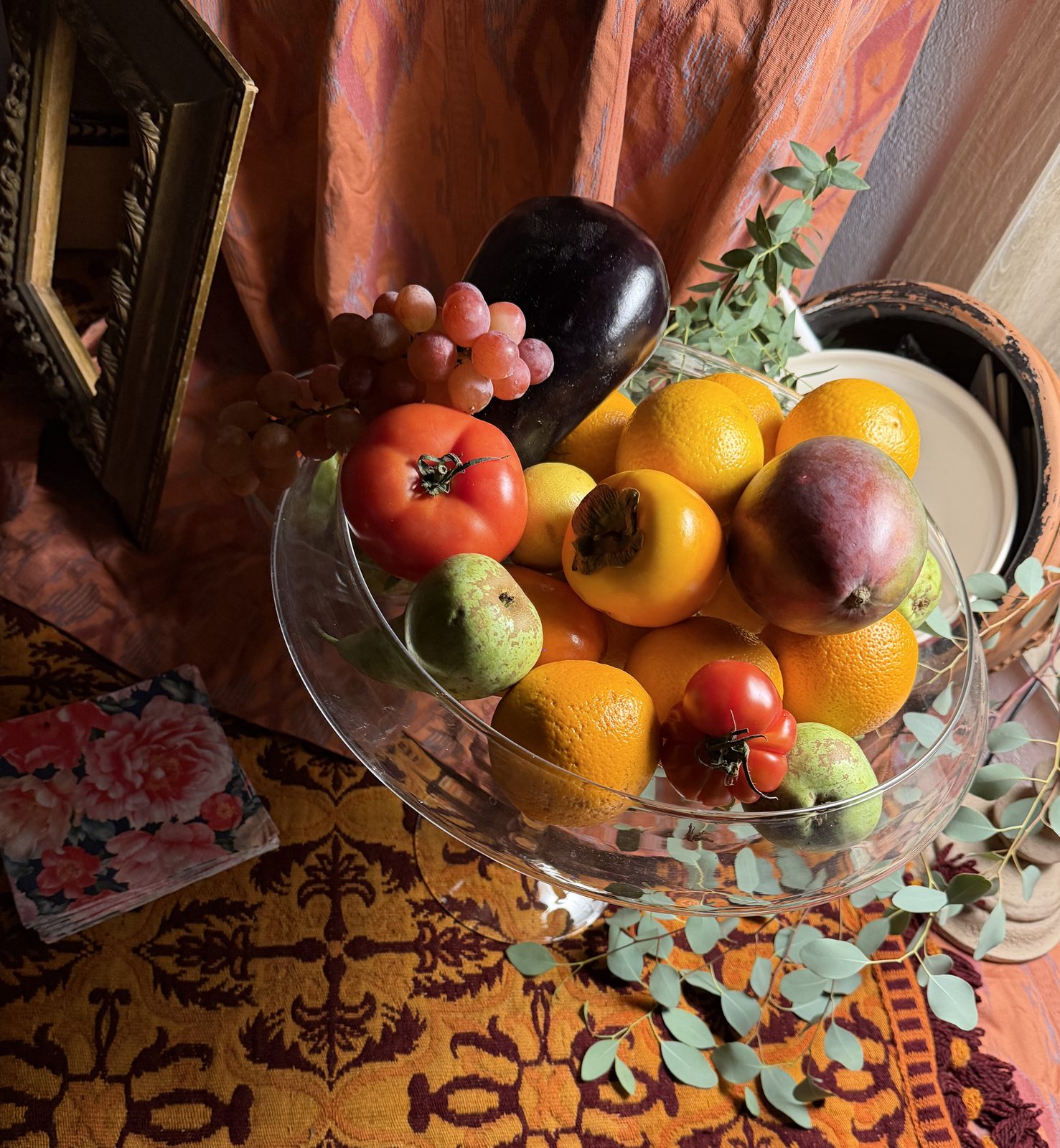Frutero de cristal con pie lleno de fruta sobre una colcha bordada